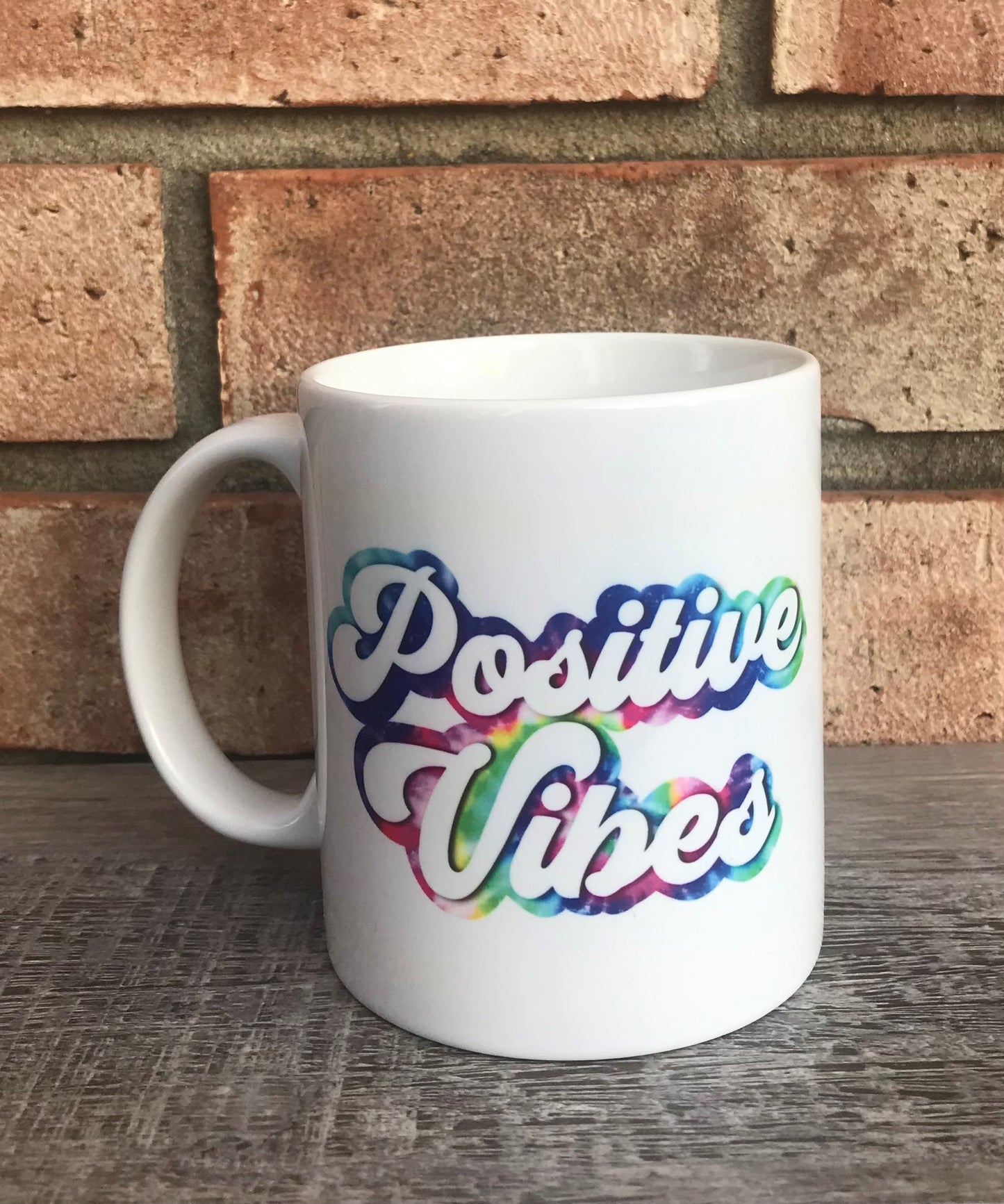 A white ceramic mug with 'POSITIVE VIBES' text in multicolored font, designed with a gradient effect.