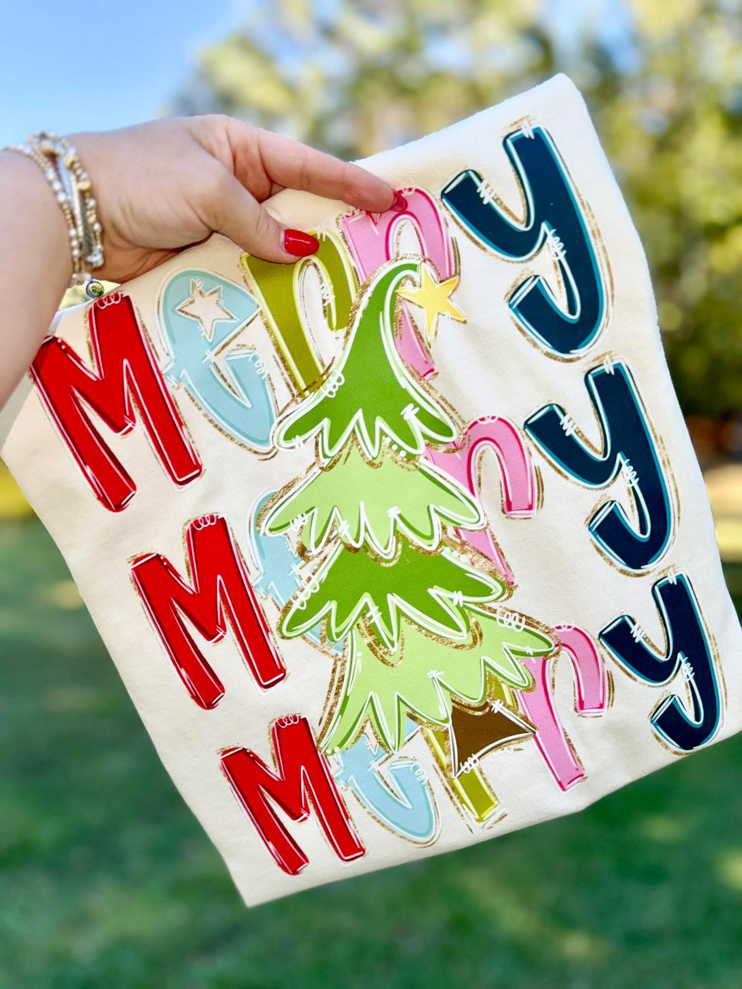 Colorful 'Merry Christmas' T-shirt held by a hand with a blurred natural background