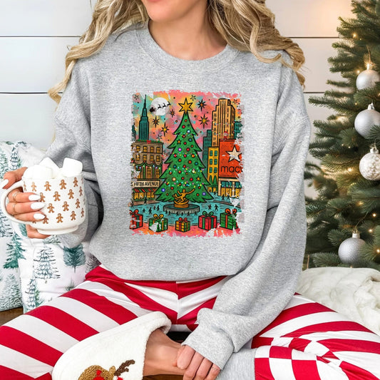 Person wearing a festive sweater with a city Christmas-themed design, holding a mug, sitting in front of a decorated Christmas tree.