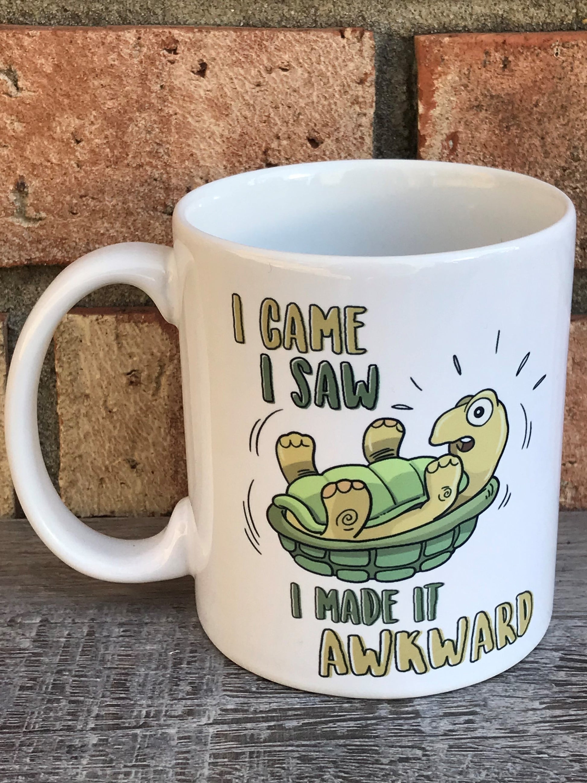 A white ceramic mug with a green turtle graphic and the text 'I came I saw I made it awkward’