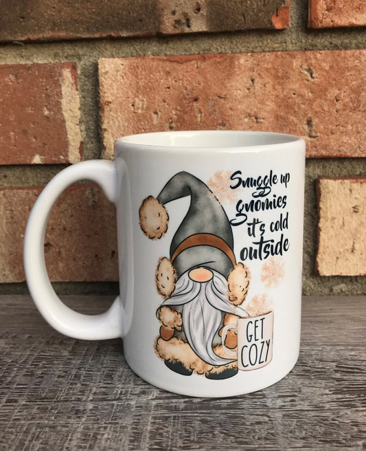 A white ceramic mug with a cartoon gnome character and the text 'Snuggle up Gnomies it's cold outside'.